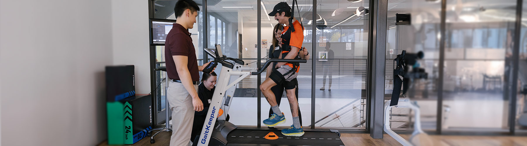 A group of Whitworth DPT students help a young adult male patient use adaptive sport equipment inside of a PT training facility.